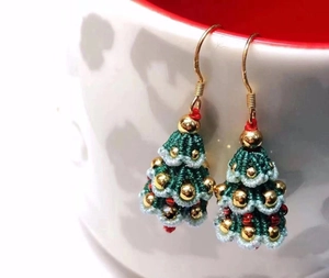 Detail of handmade crochet Christmas tree earrings hanging on a ceramic cup rim