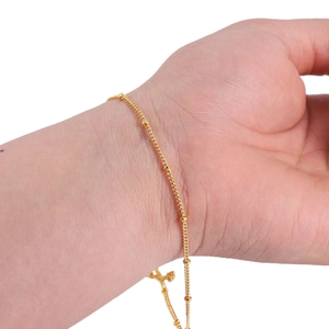 Detailed view of a slender gold-plated beaded chain bracelet worn on a female wrist
