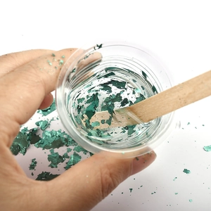 Green metallic foil flakes for DIY resin art being mixed with a wooden stir stick