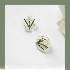 Detail of round resin earrings with white dried flowers and gold foil flakes