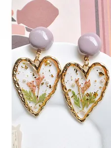 Detail of heart resin earrings with dried flowers, green leaves and gold foil flakes