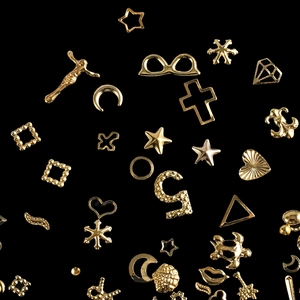 Macro shot of assorted golden alloy nail charms and resin fillers on a black background