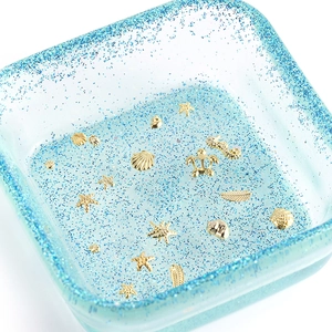 Close-up of golden nautical metal charms in blue glitter tray for DIY resin art