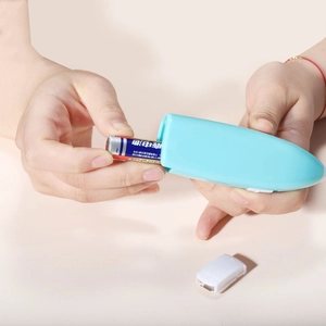 Light blue portable electric mixer showing the battery compartment being loaded by hand