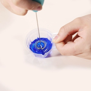 Handheld electric milk frother and resin mixer whisking blue liquid in a cup