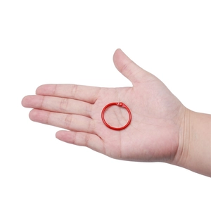 Détail d'un anneau de reliure en métal rouge de 30mm tenu en main pour montrer sa taille