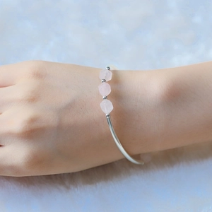 Bracciale rigido argento con perline esagonali di pietre rosa su sfondo azzurro tenue