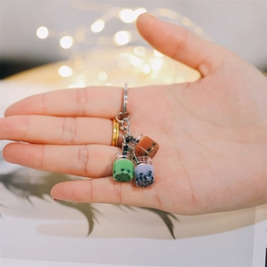 Tre portachiavi colorati con mini tazze di bubble tea e ciondoli a perla in mano