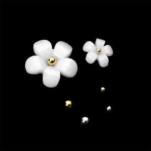 Detailed view of white resin flowers with gold beads and metallic spheres for nail art