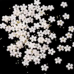 Close-up of white resin 3D flower nail charms and gold micro beads on a black background