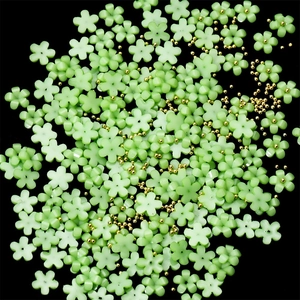 Detailed top view of light green resin 5-petal flowers and gold micro beads on black background