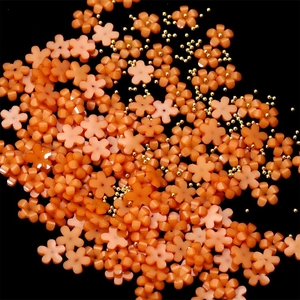 Macro shot of orange resin 5-petal flower nail charms with tiny gold center metal beads