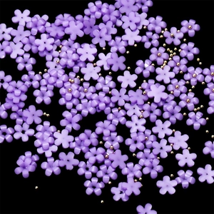 Macro shot of purple resin flowers and tiny gold beads for DIY nail art decoration