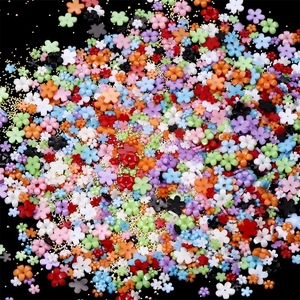 Macro shot of colorful resin flower nail art charms with golden beads on black backdrop