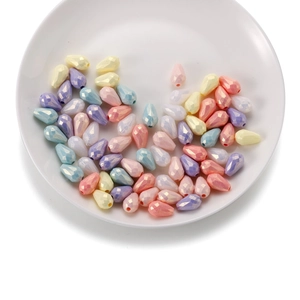Détail macro de perles acryliques facettées aux tons macaron sur une assiette en céramique
