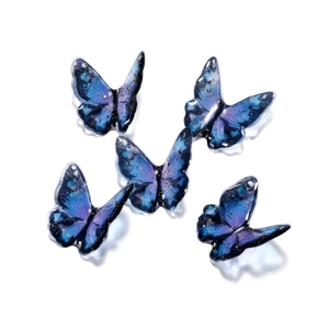 Close-up of five starry blue butterfly resin charms with gold glitter for DIY jewelry making