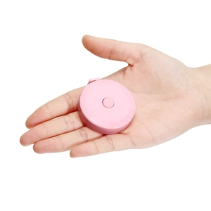 Pink mini round retractable tape measure held in palm to show portable compact size