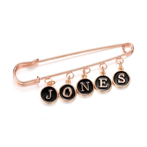 Rose gold safety pin brooch with black enamel letter charms spelling JONES