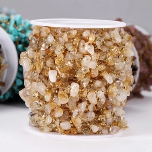 Dettaglio di perle in pietra naturale gialla con catena dorata su rocchetto per gioielli fai da te