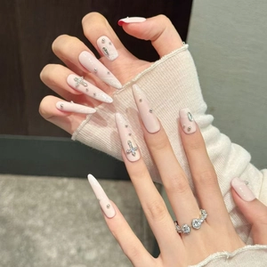Faux ongles stiletto longs avec croix argentée et perles sur base rose nude