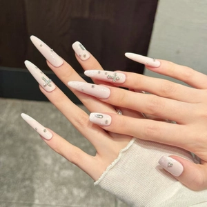 Faux ongles stiletto roses avec croix argentée et strass sur la main