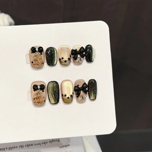 Champagne gold and dark green cat-eye press-on nails with black bows and star charms