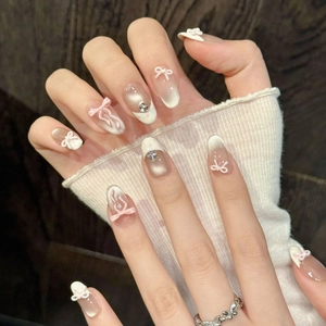 Pink gradient press-on nails with 3D bows and pearls on a textured wood background