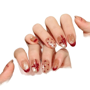 Faux ongles élégants à nœud rouge avec paillettes dorées et motifs festifs à pois