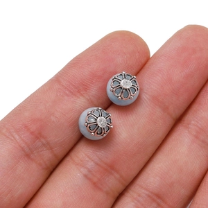 Light blue stone stud earrings with silver hollow flower caps shown on a finger