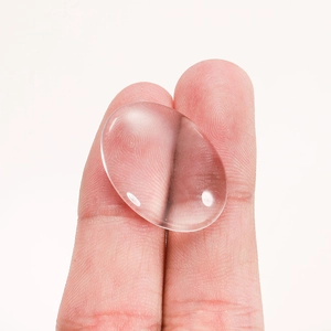 Oval clear glass cabochon for DIY jewelry making held between fingers for scale