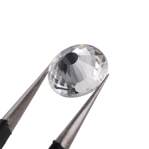 Macro shot of clear round brilliant cut glass rhinestone held by tweezers on white background
