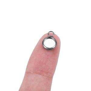 Detail of a tiny stainless steel round pendant base resting on a fingertip for DIY jewelry