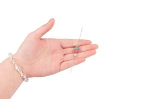 Close-up of a long silver metal beading needle with colorful decorative craft beads