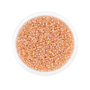 Macro shot of 2mm light orange iridescent glass seed beads in a round storage box