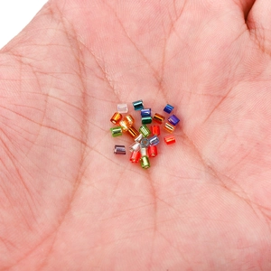 Macro shot of colorful 2mm glass bugle beads held in a hand to show small size