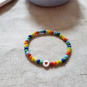 Gros plan du bracelet en perles acryliques arc-en-ciel avec une perle blanche à cœur rouge