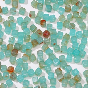 Detalle macro de cuentas acrílicas cúbicas con textura de mármol verde y marrón para joyería DIY