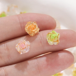 Macro shot of resin rose nail art charms with gold edges in orange, green, and pink