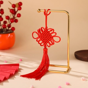 Close-up of a handmade red Chinese knot with long tassel on a gold display stand