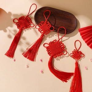 Close-up of four red Chinese knots with long tassels on a decorative wooden tray