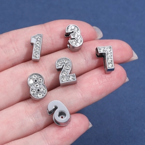 Makroaufnahme von silbernen Metallanhängern mit Strasssteinen in der Hand für den Größenvergleich