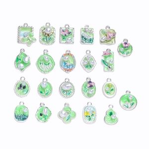 Flat lay of silver alloy charms with green enamel butterfly, starfish and pearl details