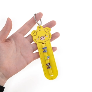 Detail of yellow pig-shaped faux leather keychain with decorative metal charms in hand