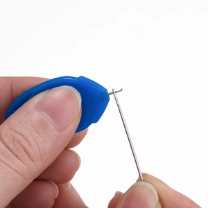 Detail of finger holding blue needle threader tool passing through a steel needle eye