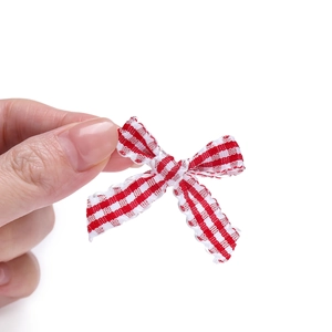 Close-up of a small red and white plaid ribbon bow held between fingers for DIY crafts
