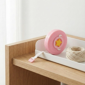 Pink heart-shaped mini measuring tape with star detail on a soft wooden desktop