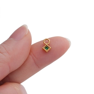 Macro detail of tiny gold plated rhombus pendant with green zircon held on fingertip