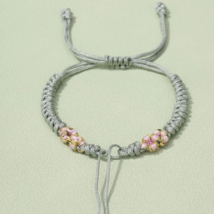 Detail of grey hand-woven peach knot bracelet with pink daisy patterns and adjustable cord