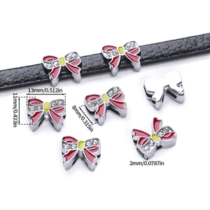 Detail of red enamel bow charms with crystals on a black leather strap for DIY bracelets
