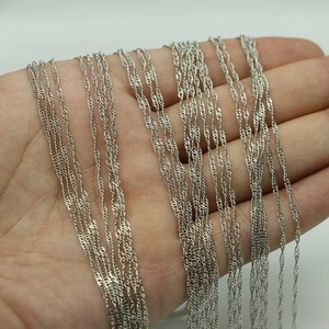 Collier chaîne à vagues argenté tenu à la main montrant une texture torsadée et un éclat métal